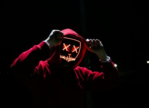 A spooky illuminated mask figure with a red hoodie in a dark setting, perfect for Halloween themes.